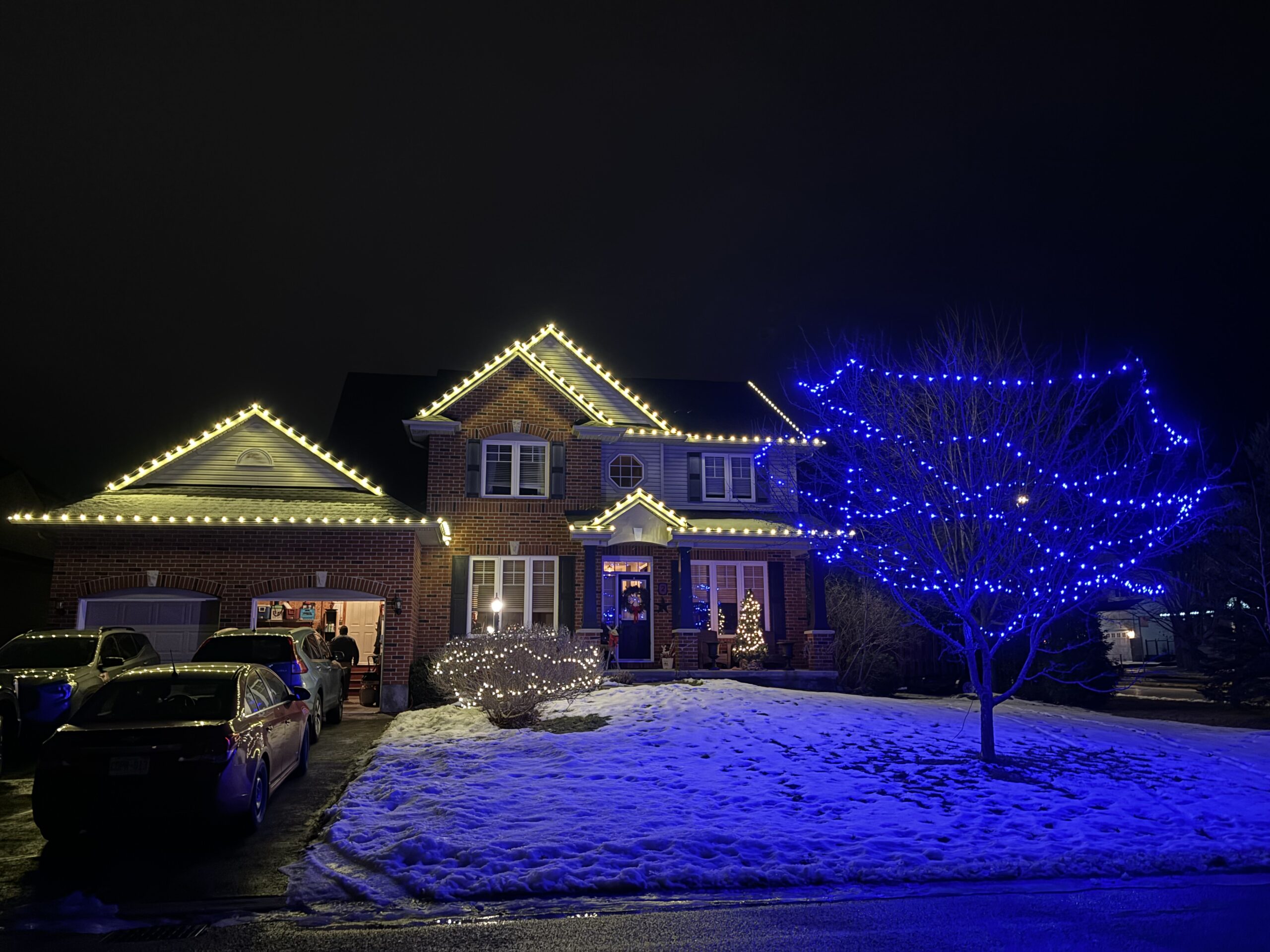 Home with white roofline lights and a blue-lit tree