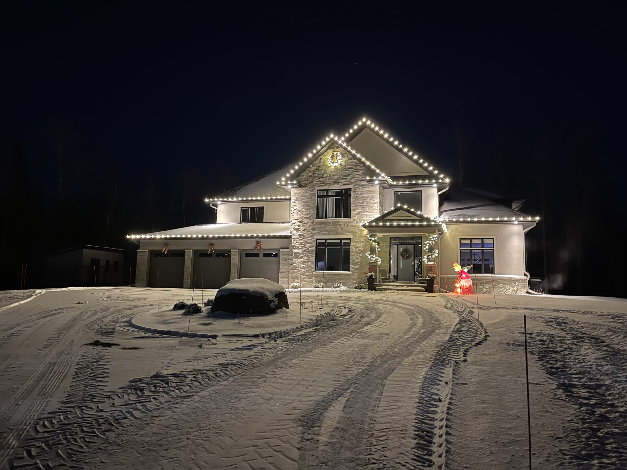 Snowy driveway and home with white Christmas lights on the peaks and eaves